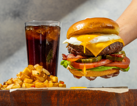 a meal of a giant cheeseburger and fries, with a soda on the side