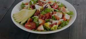 Fresh green salad topped with chopped chicken, bacon, tomatoes and slices of avocado