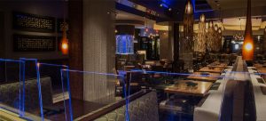 Interior view of a dining room with blue and golden lighting, and chandeliers with long tassels dangling towards the floor