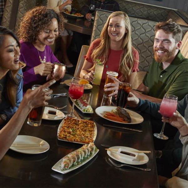 a group of people laughing and enjoying a meal and some cocktails together