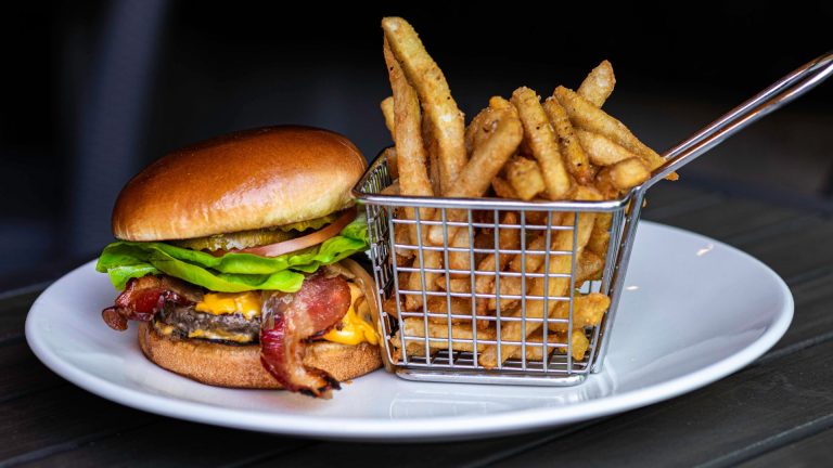 Stacked cheeseburger and a small metal crate of well-seasoned fries.