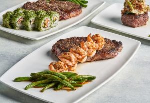 A delicious plate of shrimp, steak and green beans, next to other plates just on the edge of the frame - with sushi and another meaty-looking dish.