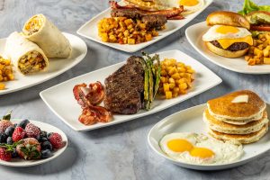 Plates full of Kona Grill brunch dishes including pancakes, fried eggs and bacon, steak and asparagus, breakfast burrito, mixed fresh berries with powdered sugar.