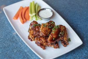 Plate of bar snacks including chicken wings, carrots and celery with a dip